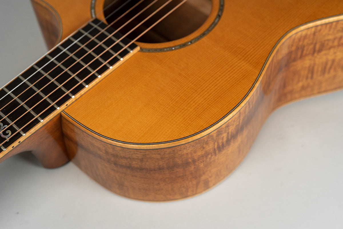 Close-up of the guitar's lower bout, showing the figured koa sides, spruce top, and dark fretboard with decorative inlay.