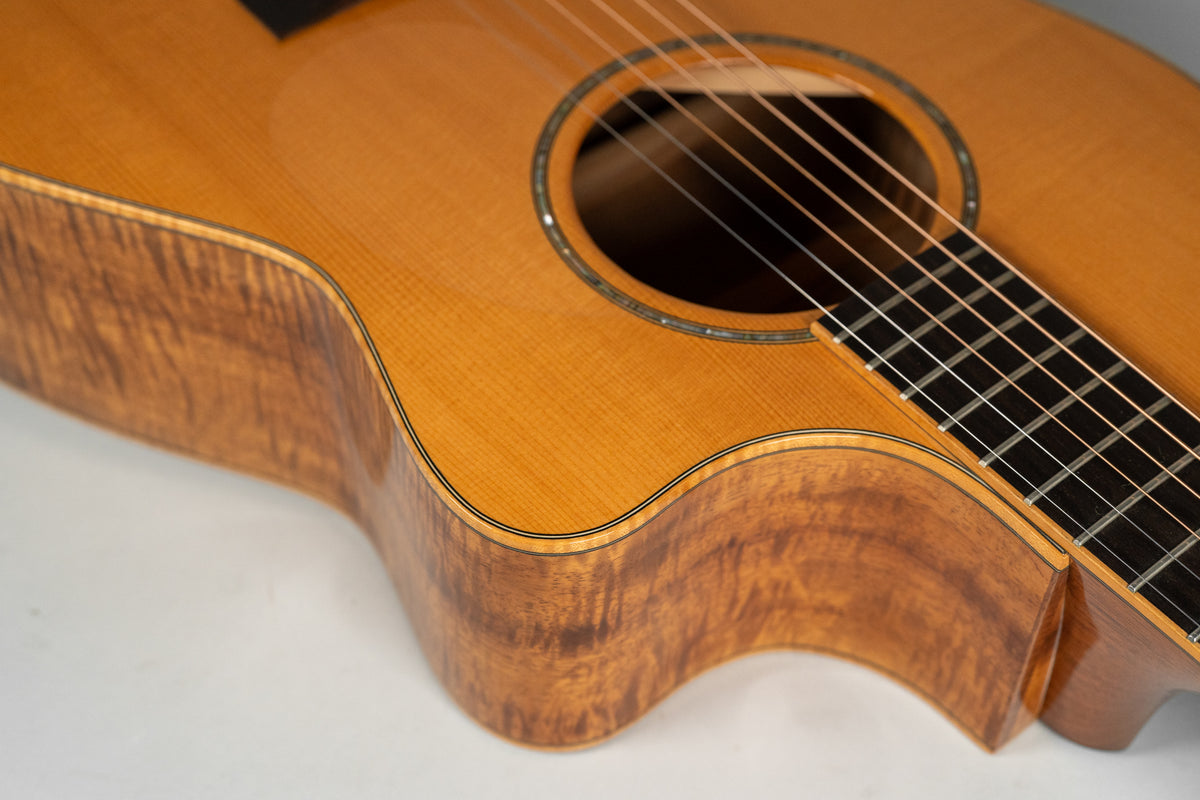 Close-up of the guitar's lower bout, showing the light brown top, dark figured sides, and soundhole with abalone inlay.