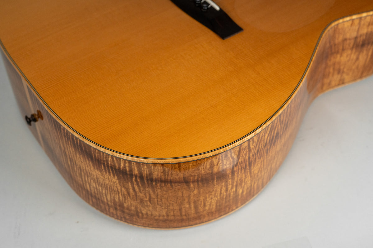 Close-up of the lower bout, showing the highly figured koa sides and a light brown top with fine grain and a black bridge.
