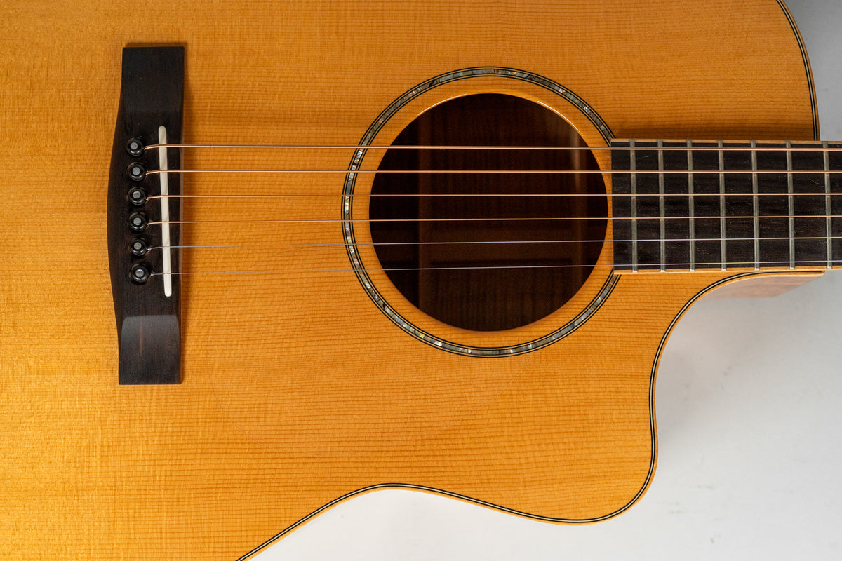 The light brown acoustic guitar body is framed from the bridge to the cutaway, showing the soundhole with abalone inlay.