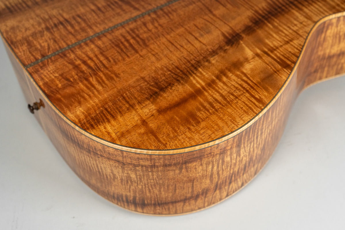 Close-up of the lower bout, showing the highly figured, wavy grain of the glossy amber koa wood back and side.