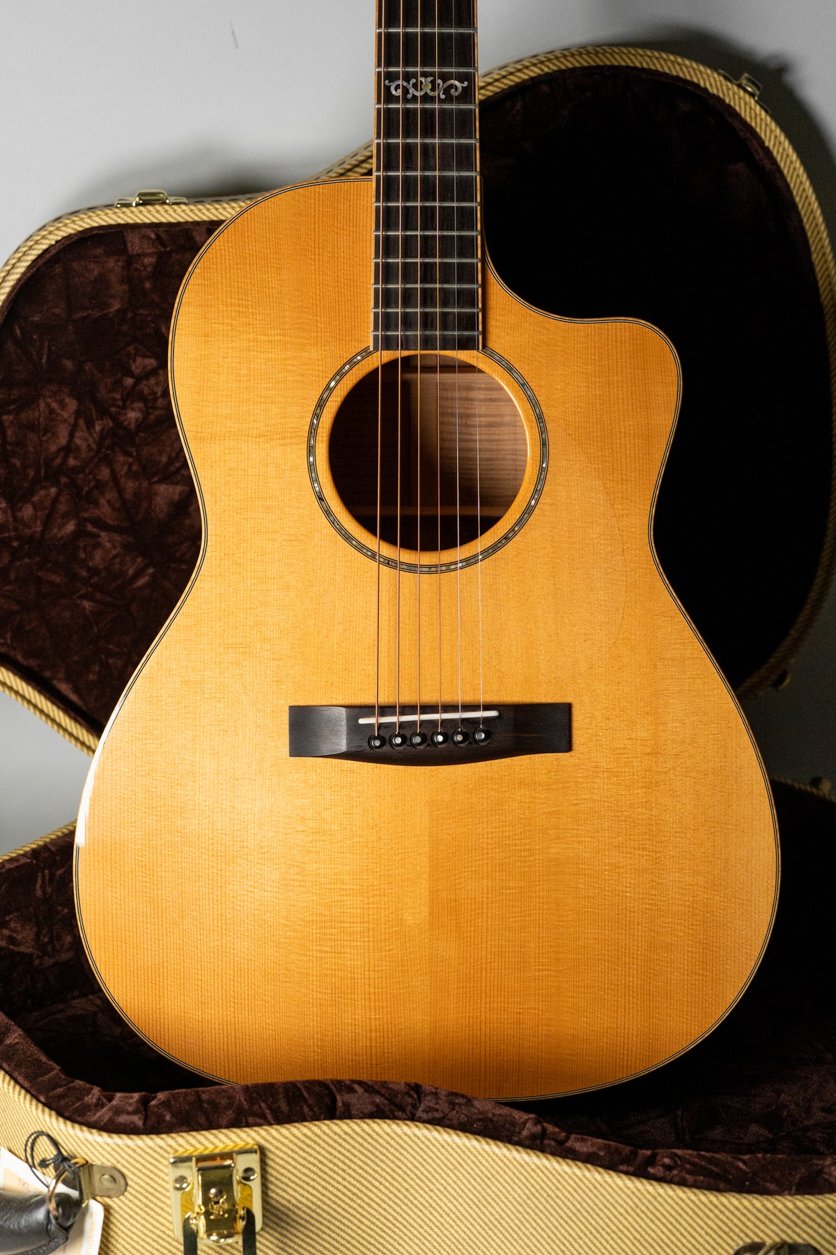 Full front view of a light blonde acoustic guitar with a cutaway, black bridge, and ornate fretboard inlay.