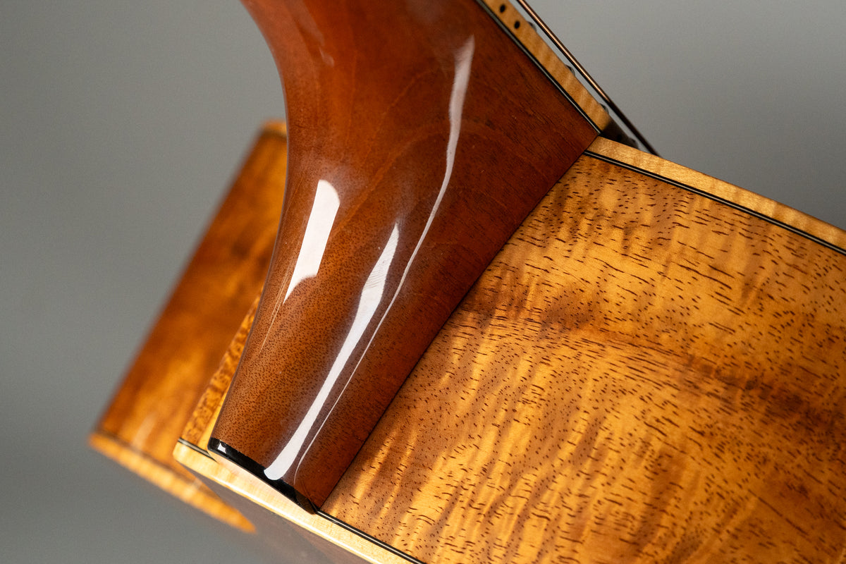 The guitar's glossy, figured koa body and neck heel are visible, showing subtle wear and a dark binding line.