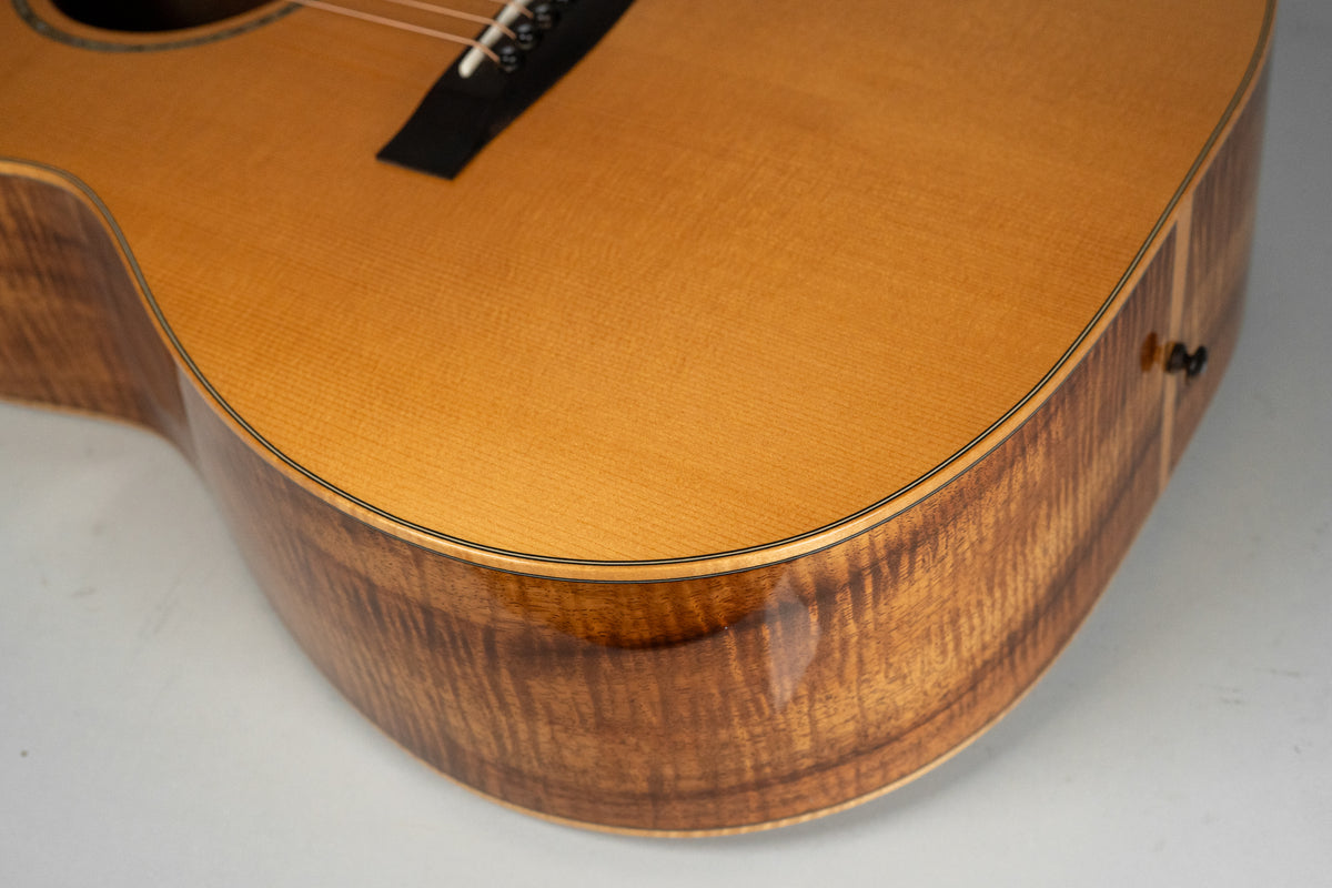 Close-up of the guitar's lower bout, showing the light-colored top and the highly figured, dark koa wood sides.