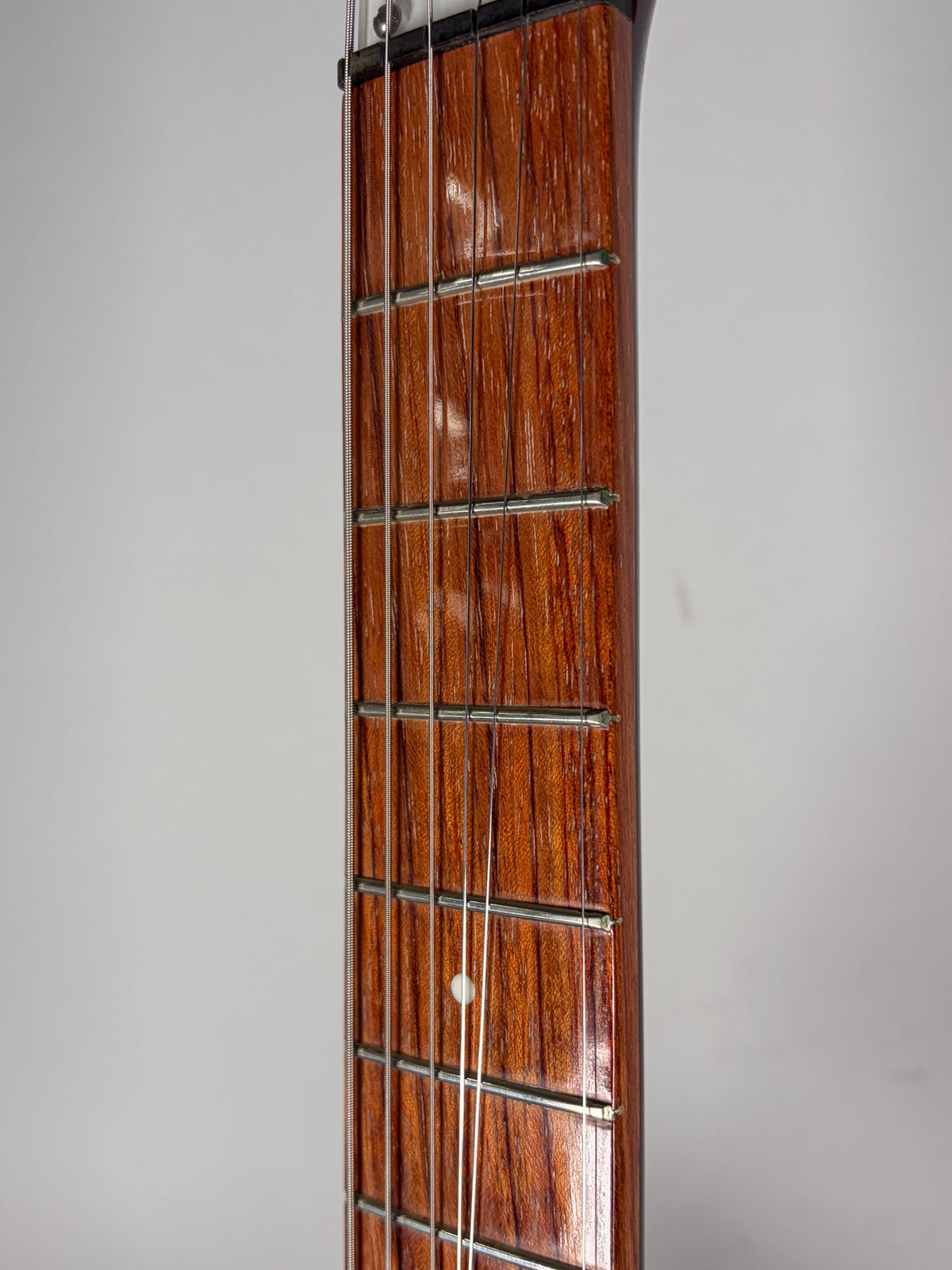 Close-up of the guitar's dark brown wooden fretboard with a single white dot inlay on the 7th fret, showing light wear.