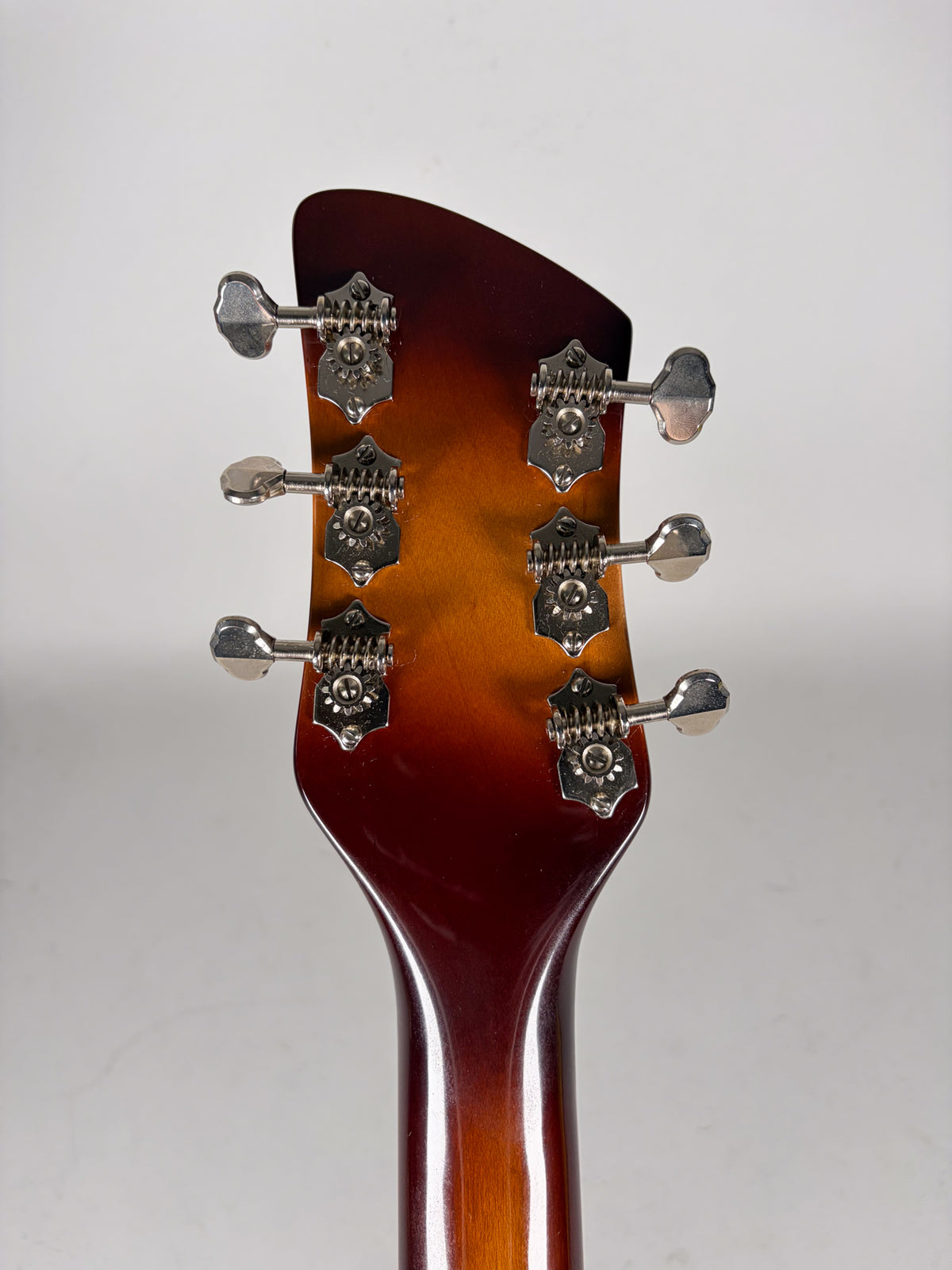 Rear view of the guitar's headstock and upper neck, showing six chrome tuners with oval buttons on a brown-to-orange sunburst finish.