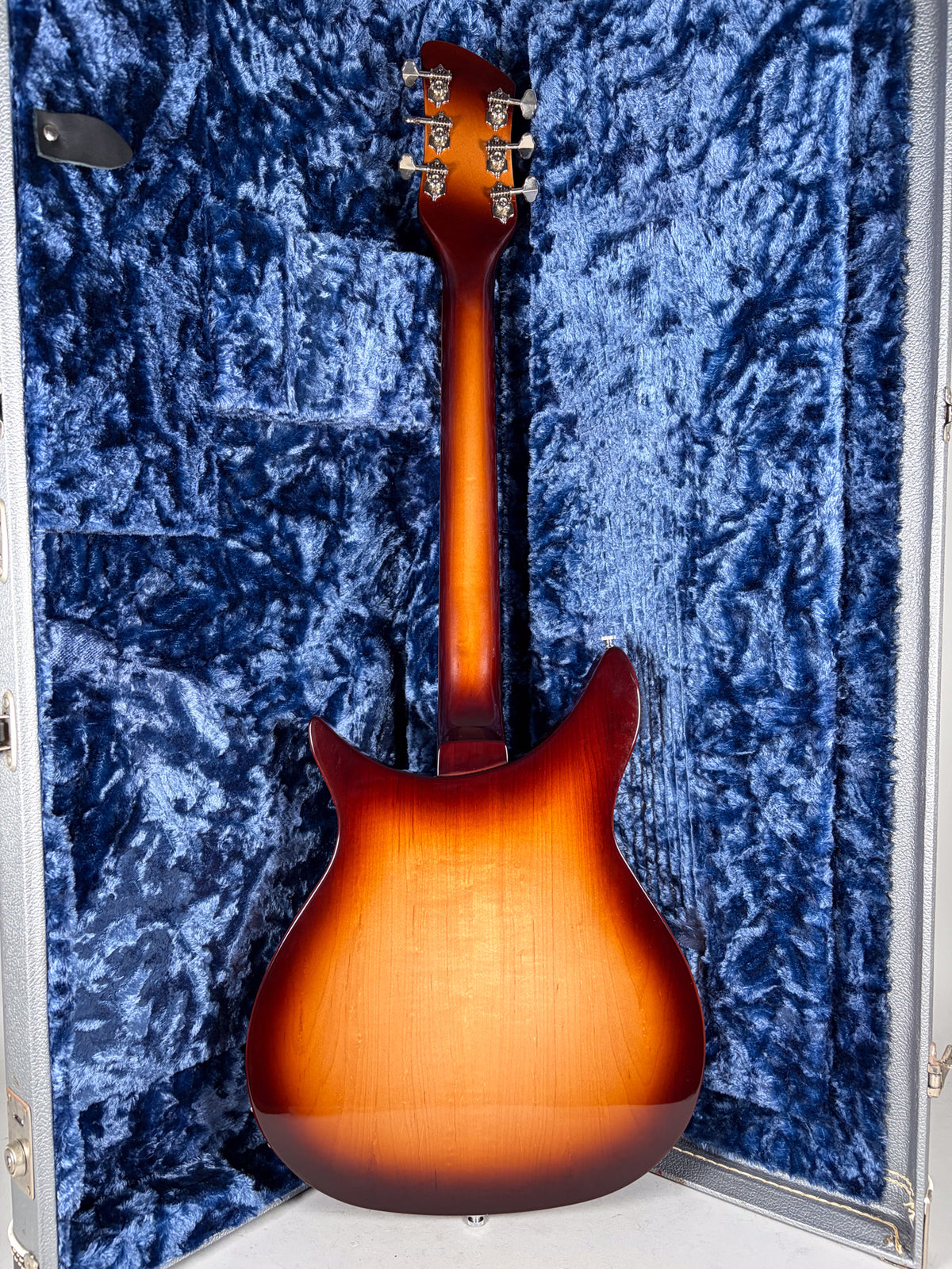 The guitar's Montezuma Brown back and neck are visible, with six chrome tuners, resting in a blue velvet-lined hard case.
