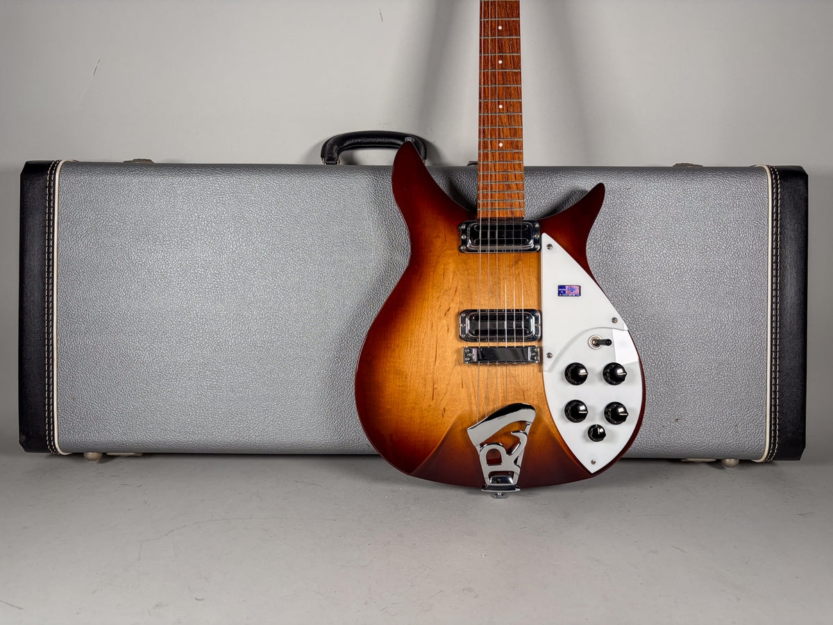 Full-body view of a sunburst guitar with a white pickguard, chrome hardware, and black control knobs, standing before a grey hard case.