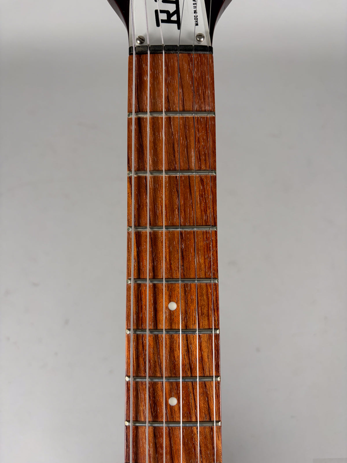 The guitar's dark brown fretboard with white dot inlays is centered, showing the headstock's top edge and nut.