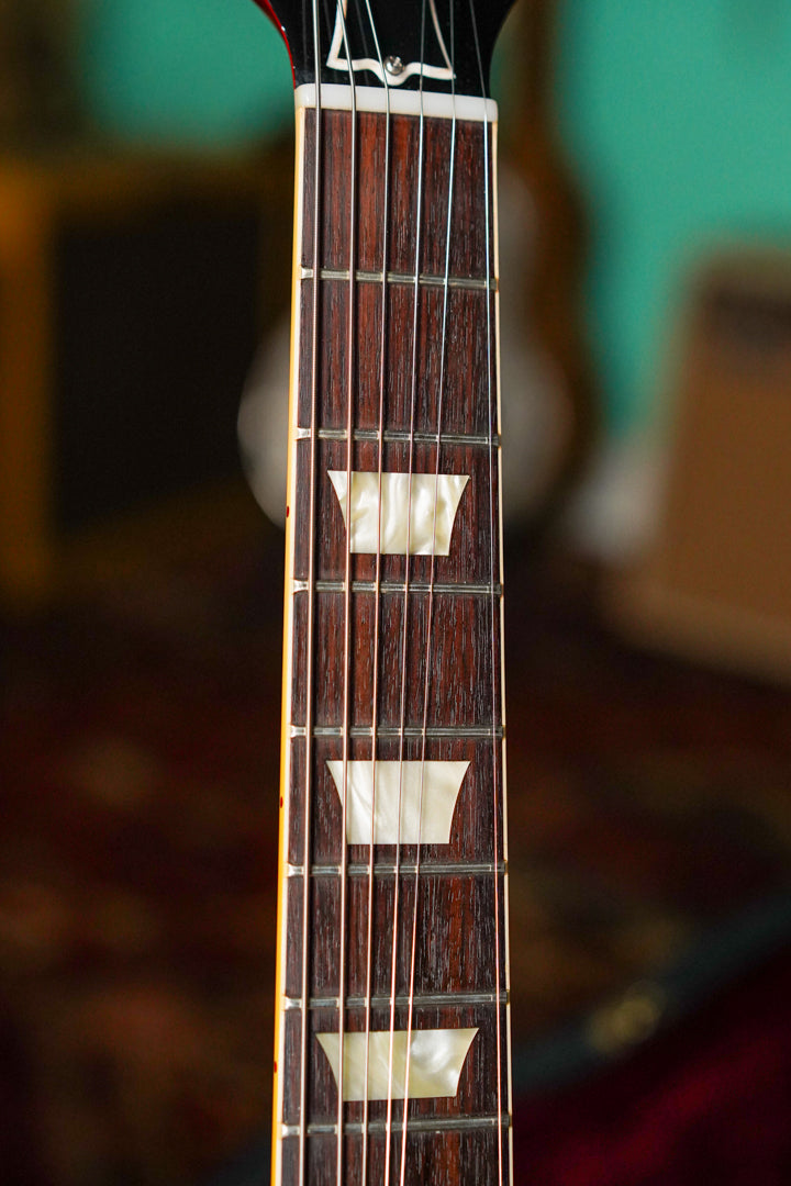 Close-up of the dark rosewood fretboard with trapezoid mother-of-pearl inlays, showing light wear on the frets and strings.