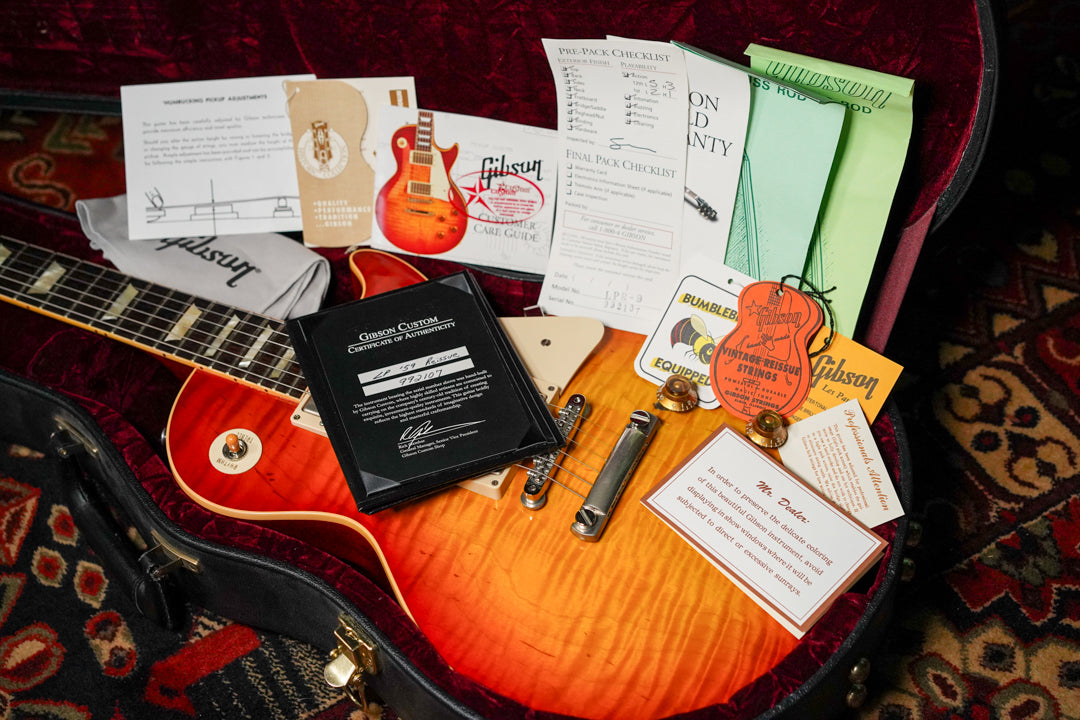 Overhead view of a sunburst Les Paul in its red-lined case, surrounded by its certificate of authenticity and various hang tags.