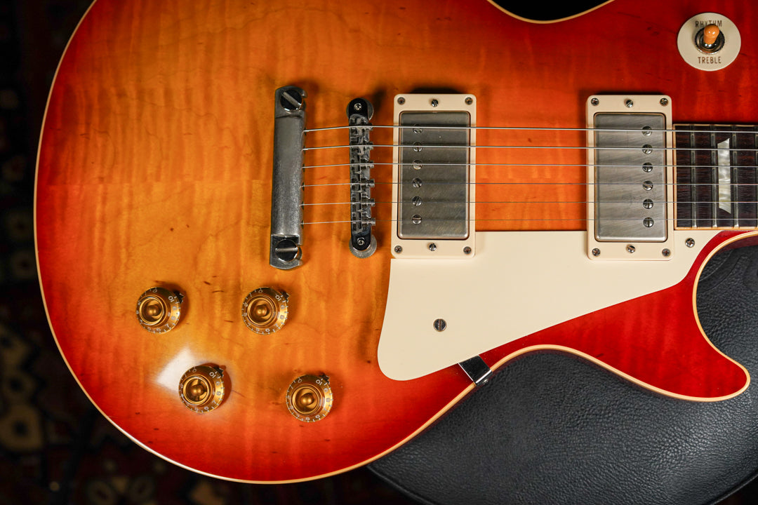 Close-up of a sunburst Les Paul's body, showing the lower bout, four gold knobs, two cream humbuckers, and a cream pickguard.