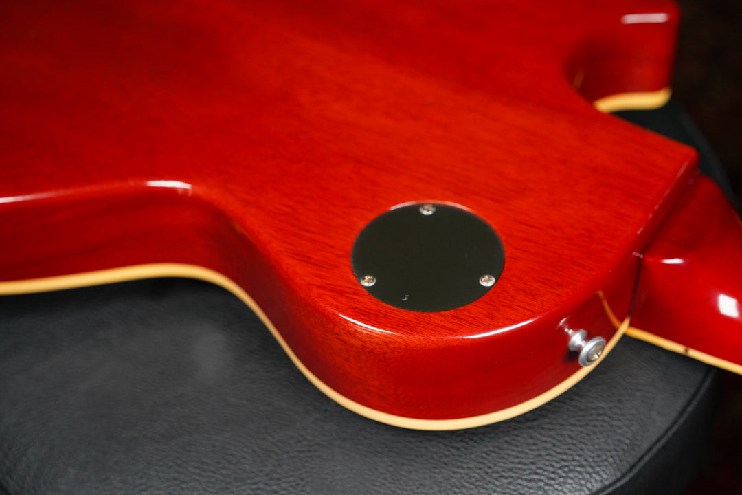 The lower bout of a cherry sunburst guitar, showing the output jack, control cavity cover, and cream binding.