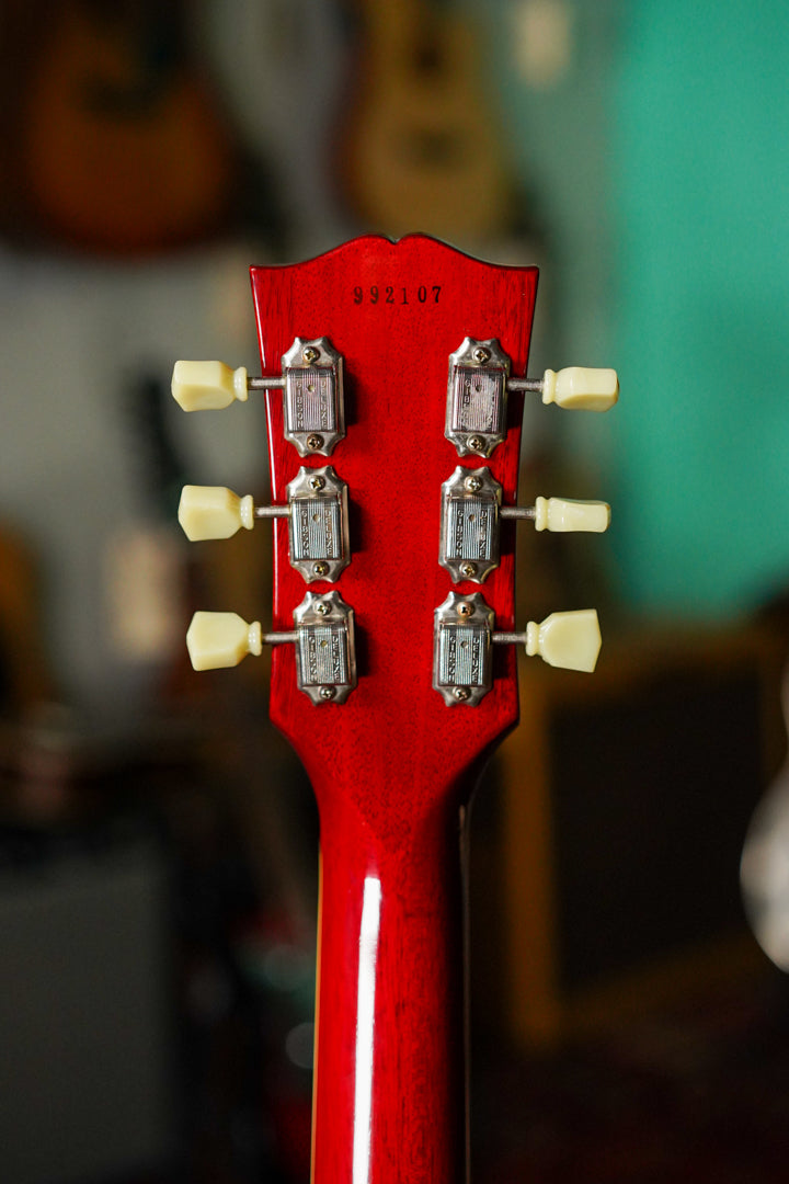 The back of a cherry red headstock with six cream tuning pegs and chrome tuners, showing some light wear.
