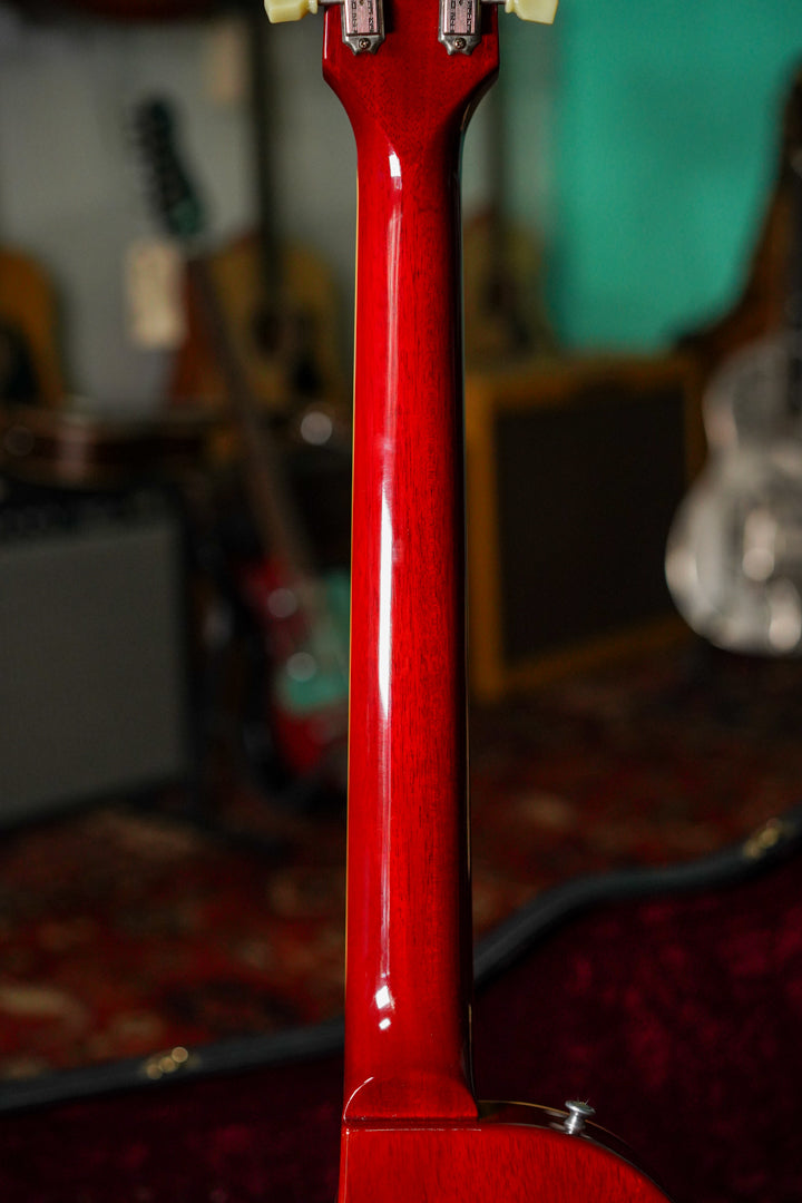 The back of the guitar's glossy, deep red neck and headstock, showing two tuning pegs and a strap button, with wood grain visible.