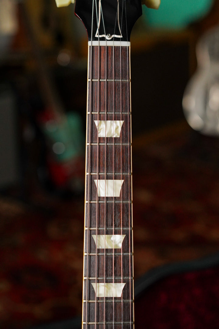 Close-up of the dark rosewood fretboard with trapezoid mother-of-pearl inlays, showing light wear and a bone nut.