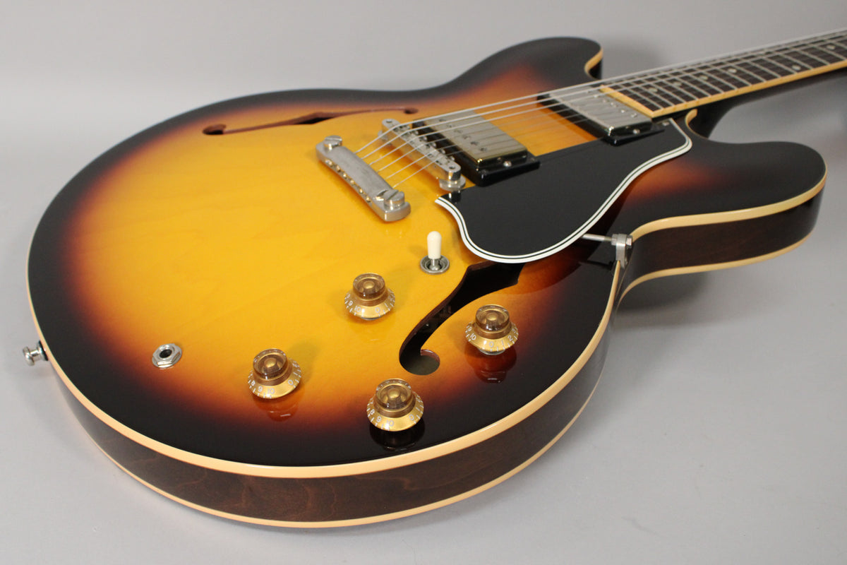 The sunburst semi-hollowbody guitar's lower bout and cutaway, showing the bridge, black pickguard, and four amber control knobs.