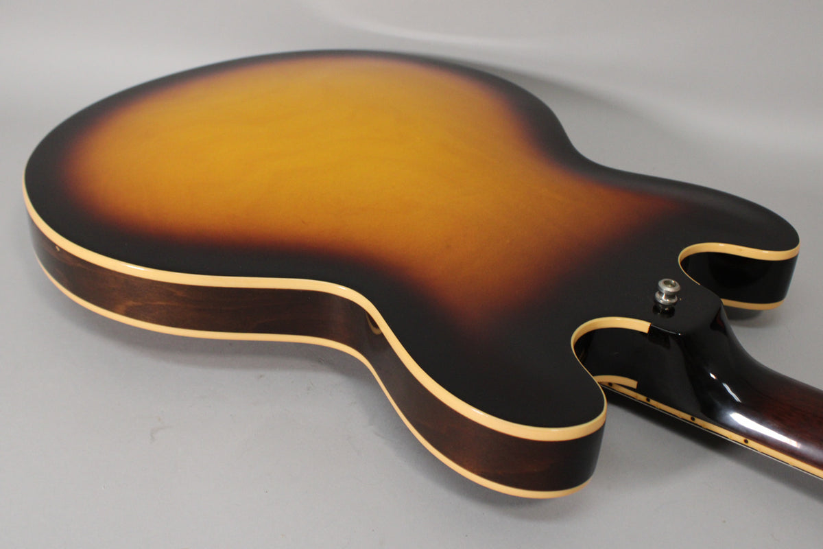 The back of a sunburst guitar, showing the lower bout and cutaways, with a strap button and neck heel.