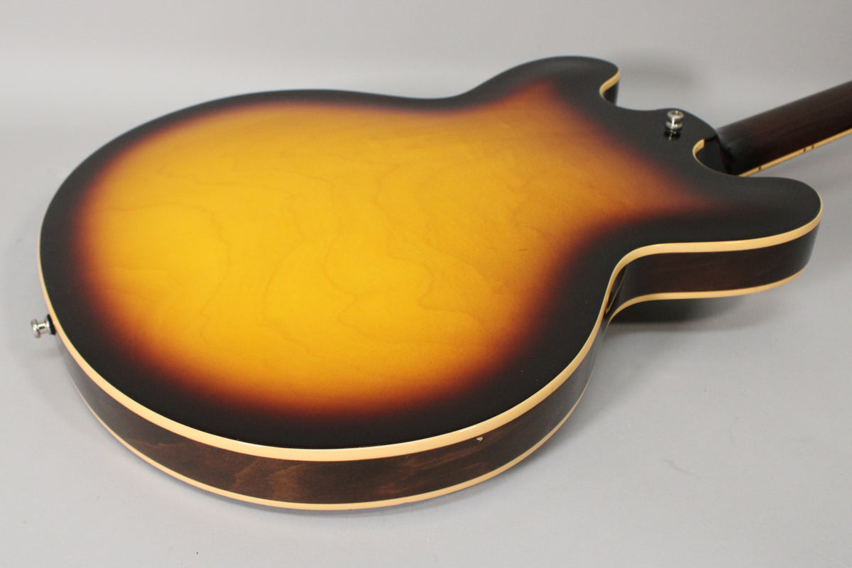 The back of a sunburst semi-hollow guitar, showing the dark brown sides, light binding, and a small ding on the lower bout.