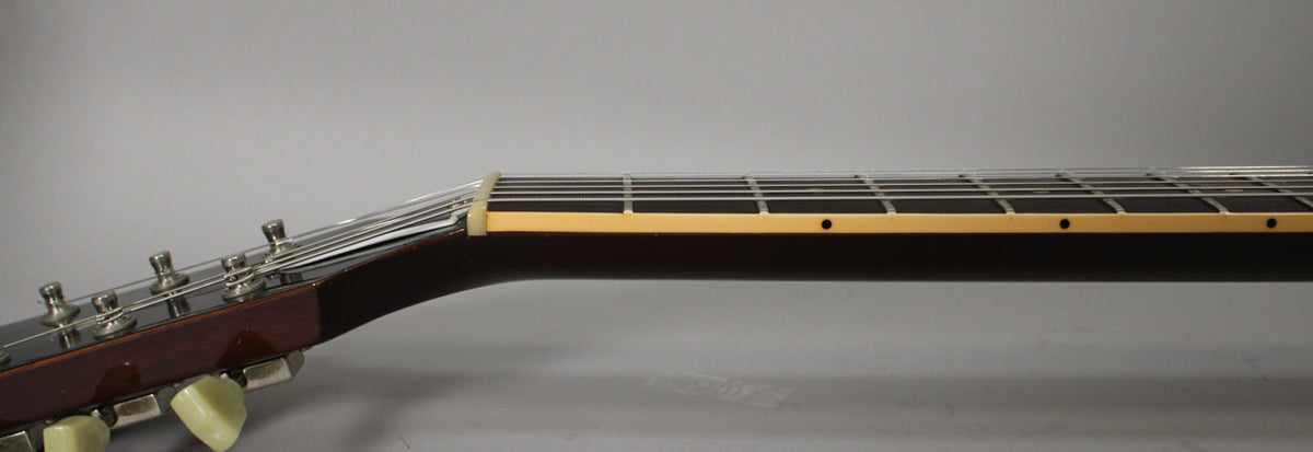 The guitar's dark brown neck and headstock are viewed from the side, showing the cream binding, frets, and tuning pegs.