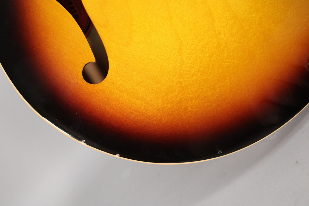 Close-up of the lower bout of the sunburst guitar body, showing the f-hole and some minor finish chips along the bottom edge.