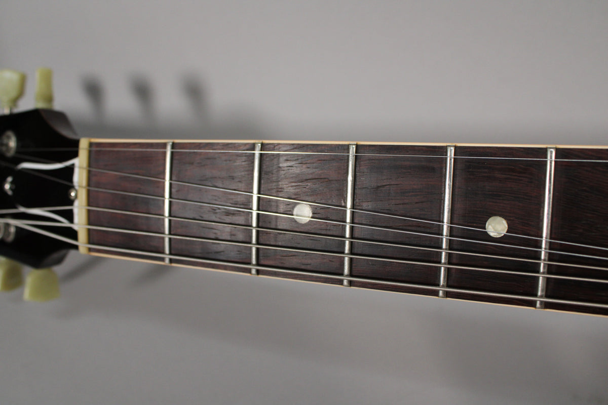 Close-up of the dark rosewood fretboard with white binding, showing frets 1-7, dot inlays, and the cream tuning pegs.
