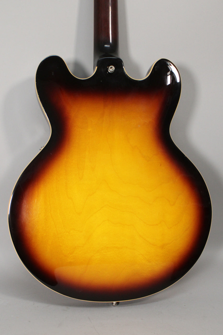 The back of a sunburst semi-hollow guitar, showing the dark brown neck heel and body with a few small dings.