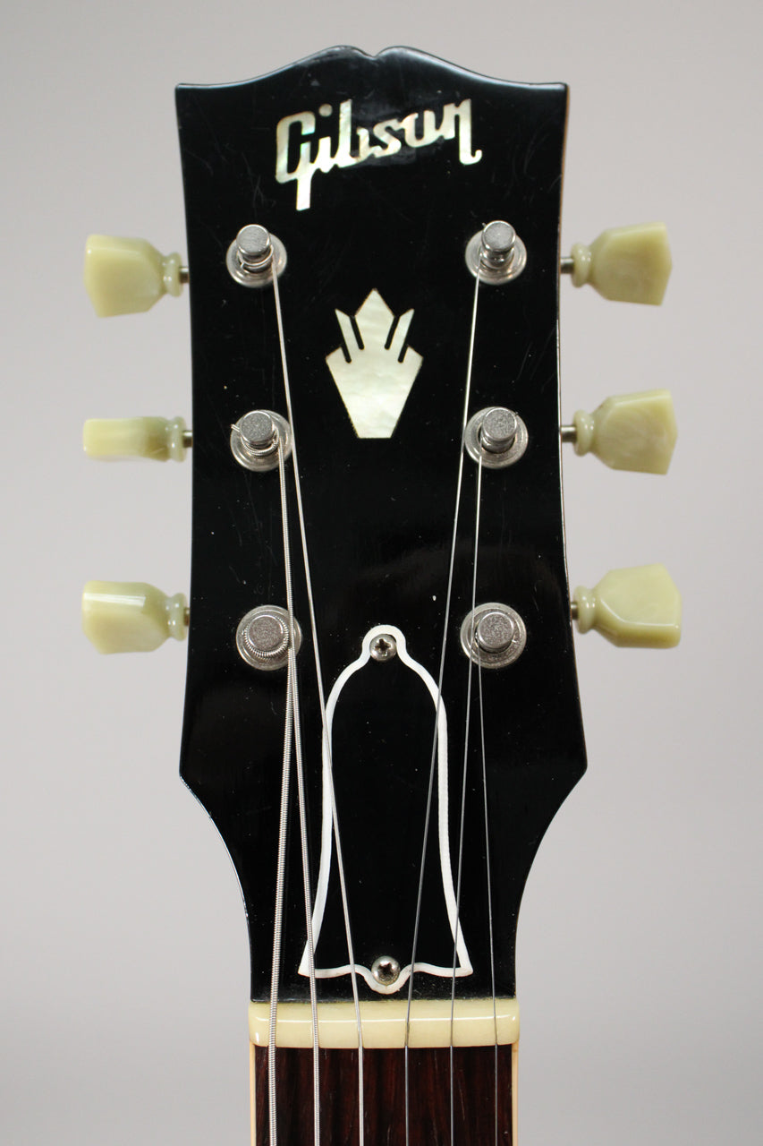 Close-up of the black headstock with mother-of-pearl inlays, six cream tuning pegs, and light string wear around the tuning posts.