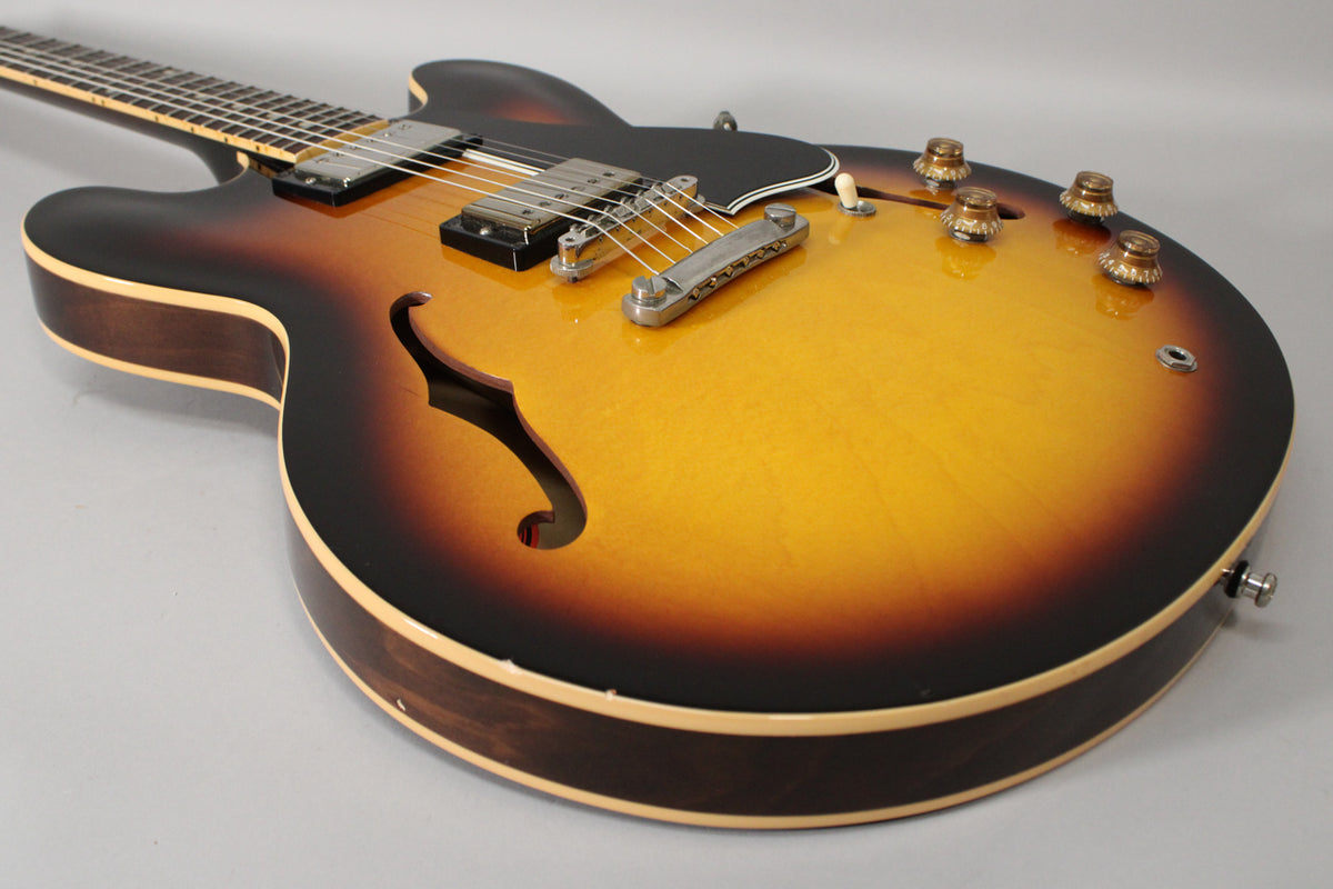 The sunburst semi-hollowbody guitar is angled left, showing its lower bout, f-hole, pickups, bridge, and four amber control knobs.