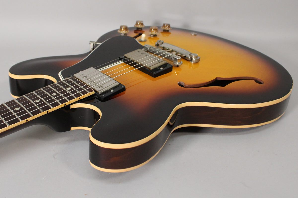 The sunburst semi-hollow guitar is angled, showing its dark brown sides, cream binding, f-hole, and chrome hardware.