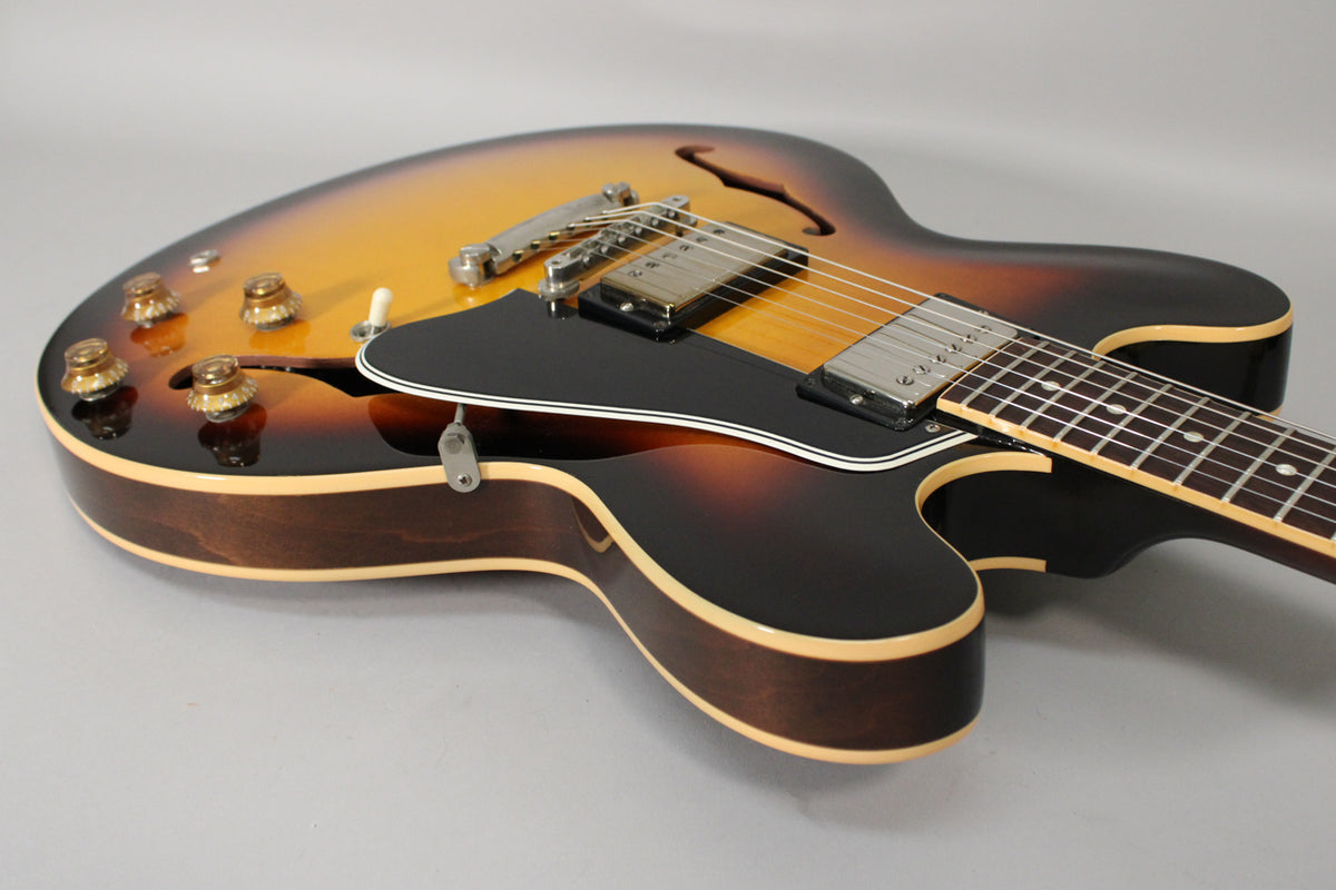 The sunburst semi-hollowbody guitar is angled right, showing its upper bout with four amber knobs, black pickguard, and two humbuckers.