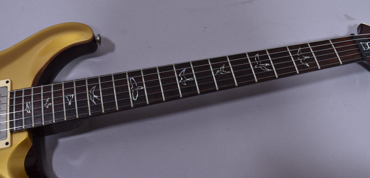 Close-up of the guitar's dark fretboard with mother-of-pearl bird inlays, showing the gold body and cream pickup on the left.