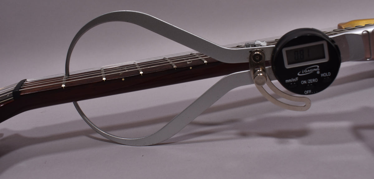 A digital caliper measures the guitar's dark rosewood fretboard, showing a reading of 0.81.