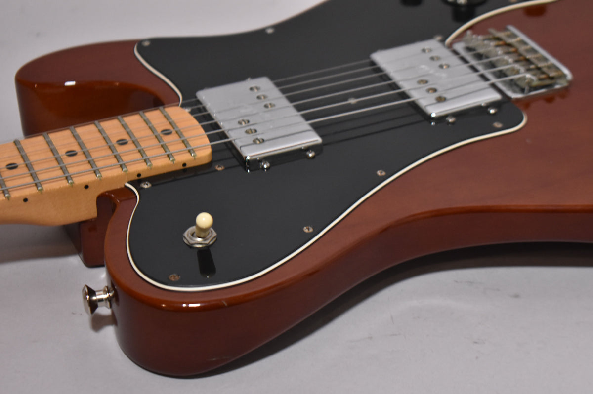 Close-up of a glossy mocha electric guitar body with a black pickguard, two chrome humbuckers, and a maple fretboard.