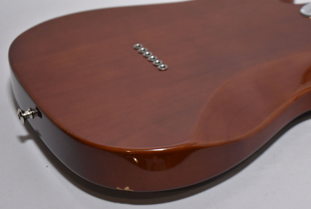 The guitar's mocha body is angled, showing the back with six string ferrules and a chipped finish near the strap button.