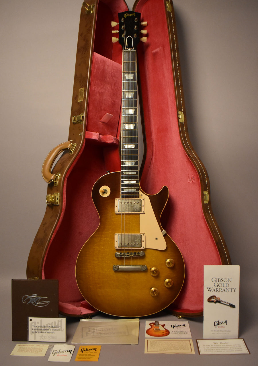 Full-length, front view of a sunburst Les Paul with cream binding, pickguard, and pickup rings, in its open, red-lined brown case.