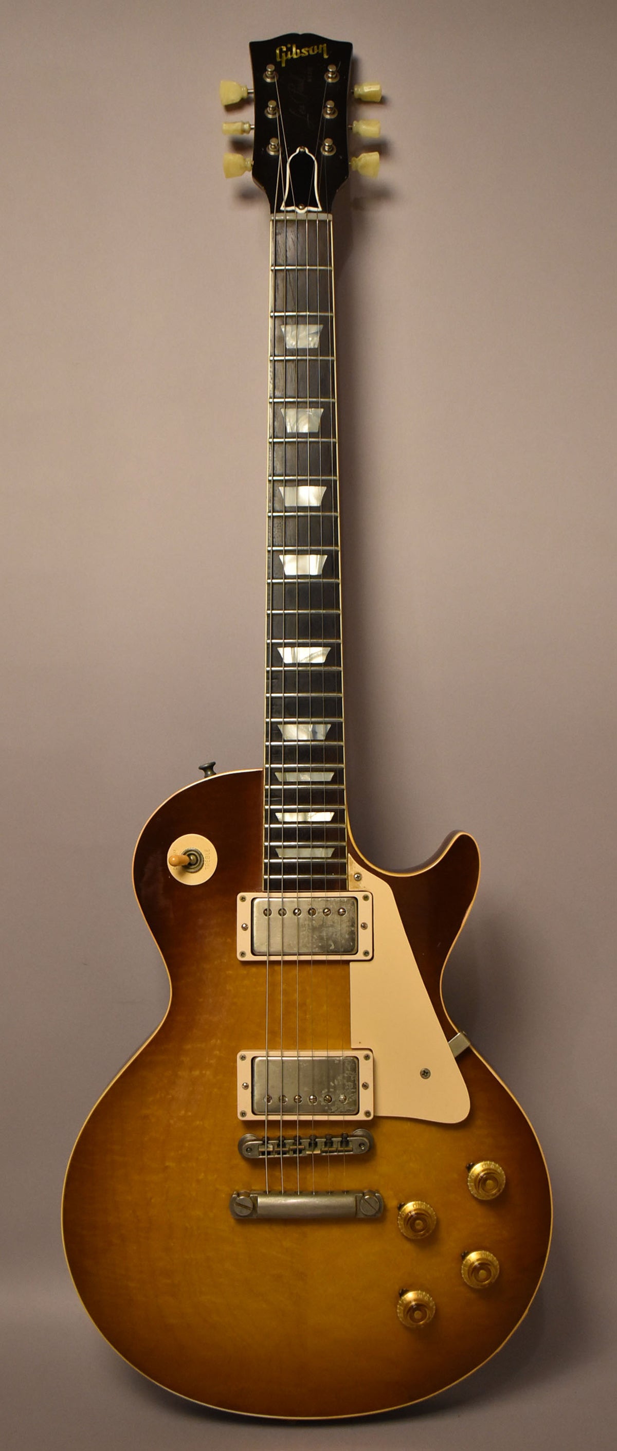 Full-length, front view of a sunburst Les Paul with a dark headstock, trapezoid inlays, and aged nickel hardware.