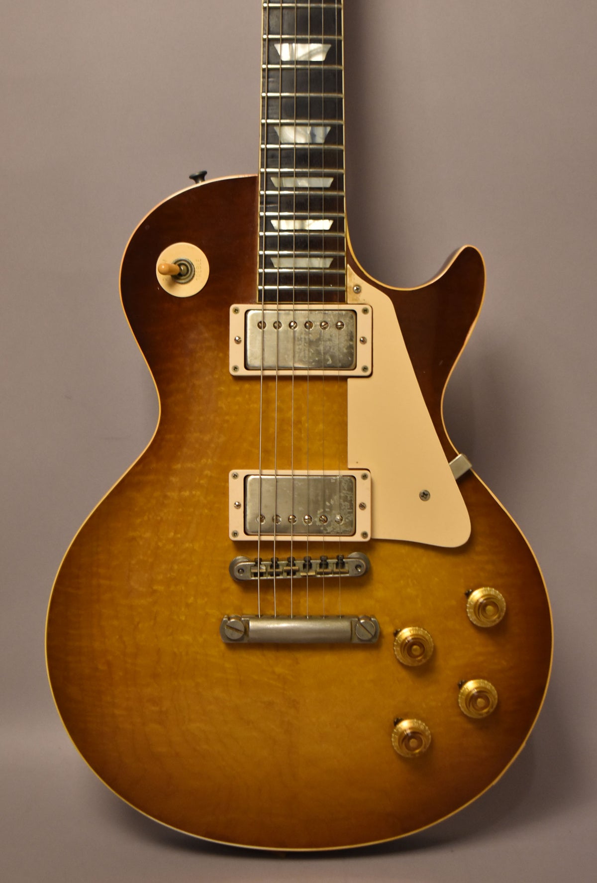 The sunburst Les Paul's body and fretboard are framed, showing two humbuckers, a cream pickguard, and four gold control knobs.