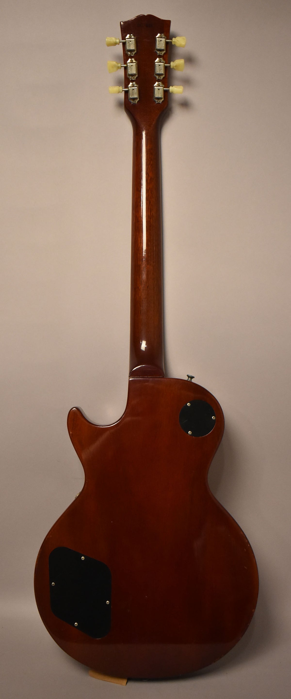 The guitar's back is a dark reddish-brown with a glossy finish, showing two black control plates and six cream tuning pegs.