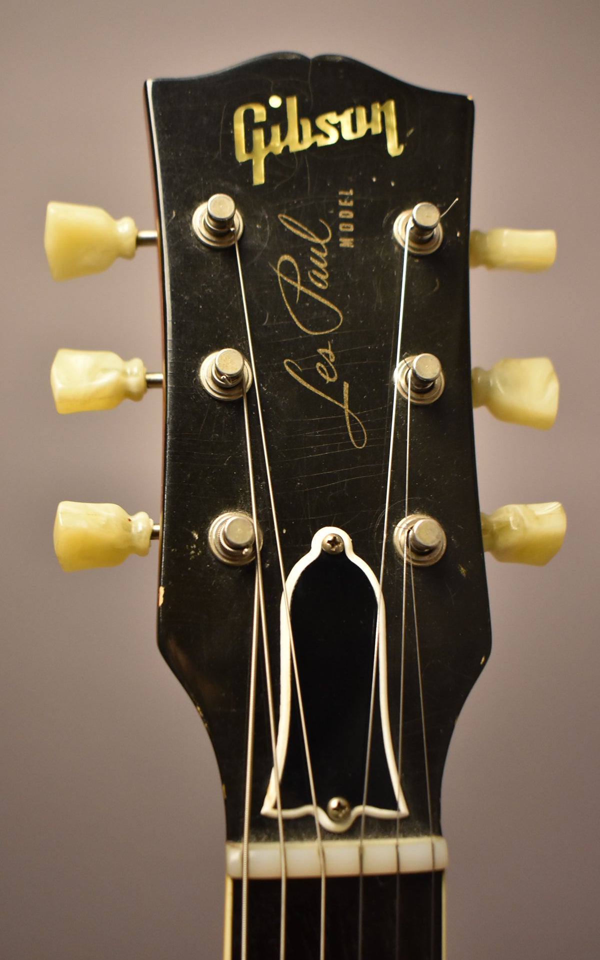 Close-up of the black headstock with gold lettering, six cream tuning pegs, and visible finish checking and light wear.