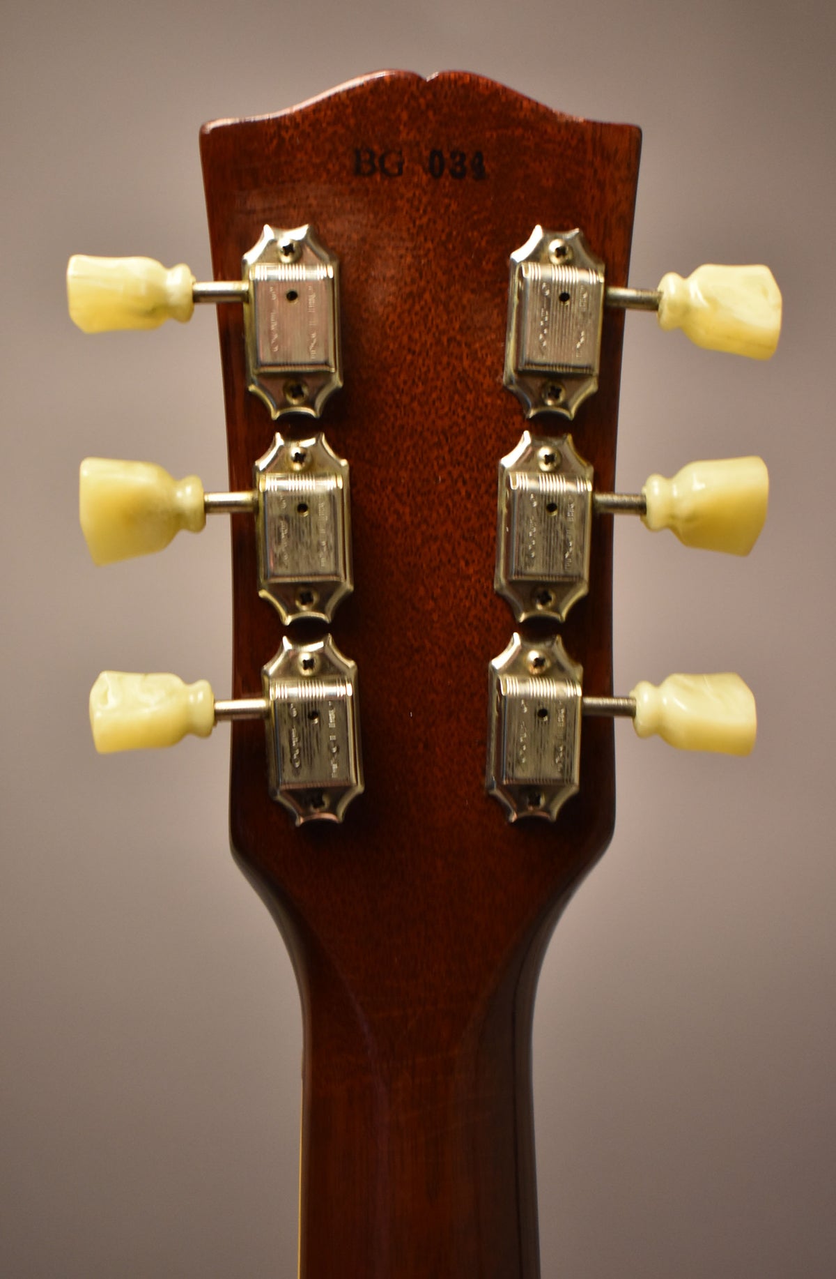 Rear view of the guitar's headstock and upper neck, showing six cream-colored tuning pegs and chrome tuners on a dark brown finish.