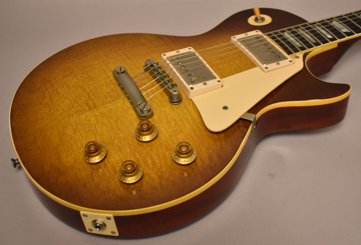 The guitar's sunburst body, with visible wood grain, features four gold top hat knobs, a cream pickguard, and aged nickel hardware.