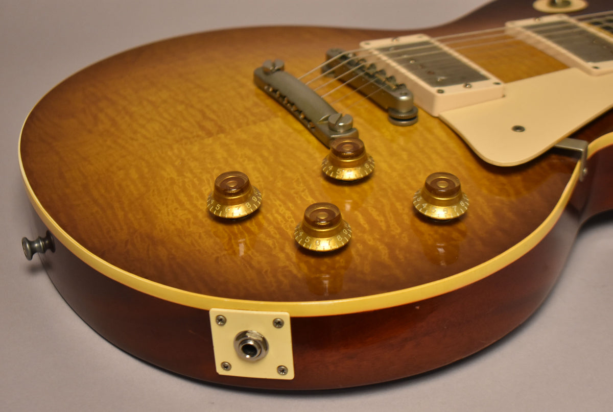 Close-up of the lower bout, showing the sunburst finish, four amber control knobs, output jack, and bridge.