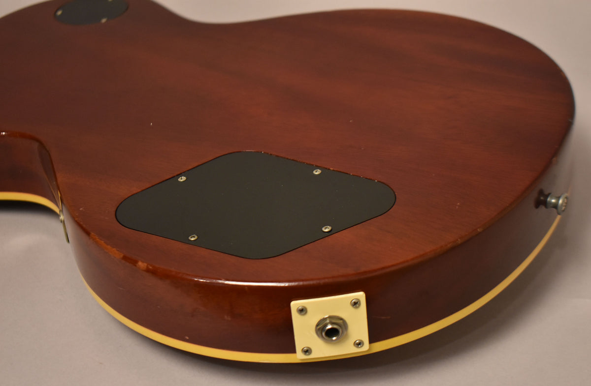 Close-up of the guitar's dark brown back, showing a black control cavity cover and a cream output jack plate with some wear on the body edge.
