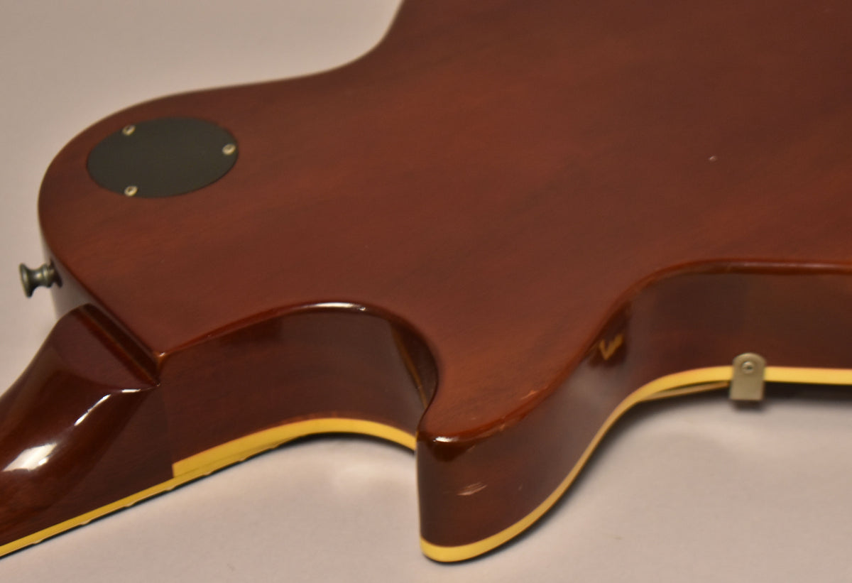 The guitar's dark brown back and sides, with cream binding, show light wear and a black control cavity cover.