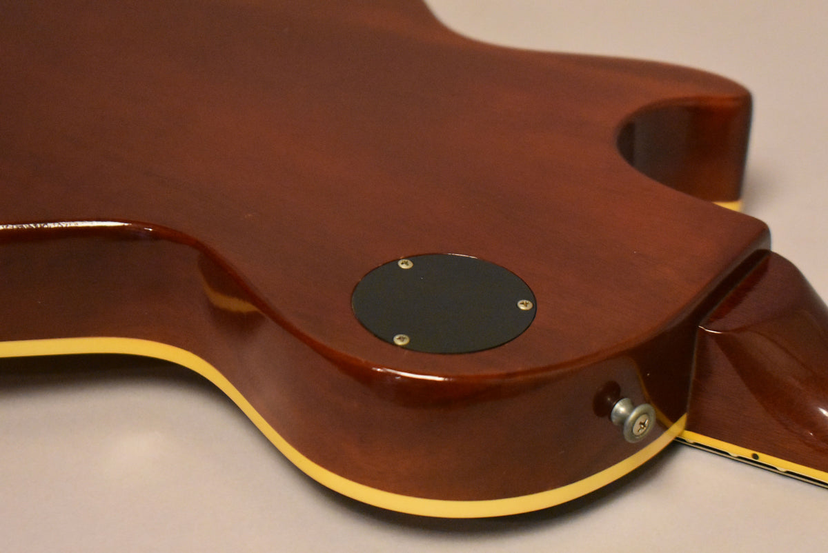 The guitar's dark brown back and side are visible, with a black control cavity cover and a chrome strap button.