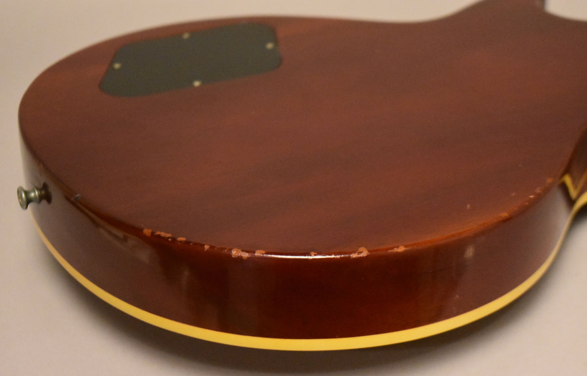 The guitar's lower bout, seen from the back, shows a dark sunburst finish with significant chipping along the binding.