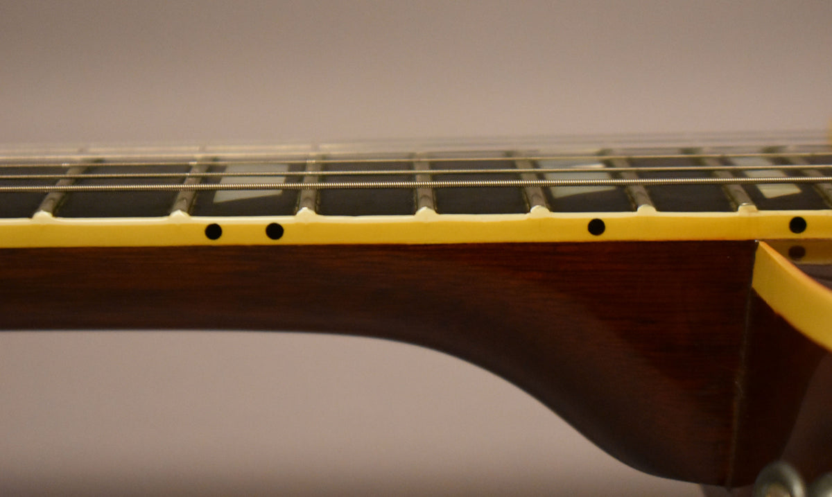 The guitar's dark brown neck and fretboard are visible from the side, with cream binding and black dot markers.