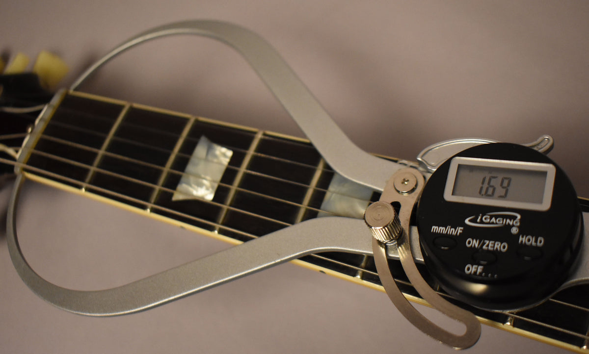 A digital caliper measures the fretboard width at 1.69 inches, showing trapezoid inlays and cream binding.
