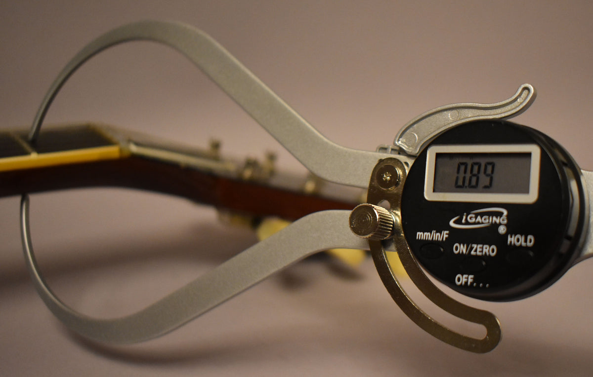 A digital caliper measures the guitar's nut width at 0.89 inches, with the dark brown neck and cream binding visible.